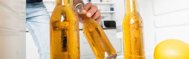 Gewassen beeld van de mens het nemen van natte fles bier uit open koelkast op wazige achtergrond, banner  - Foto, afbeelding