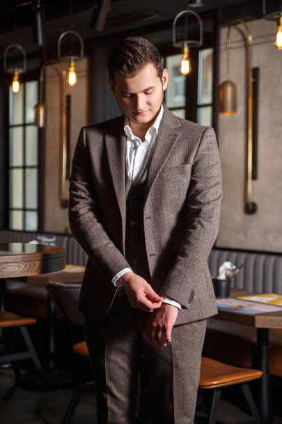 Stijlvolle jongeman in elegant driedelig pak in de buurt van bar in restaurant interieur. - Foto, afbeelding