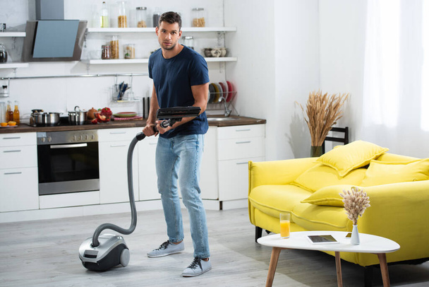 Man holding brush of vacuum cleaner near devices and glass of orange juice on coffee table  - Foto, immagini
