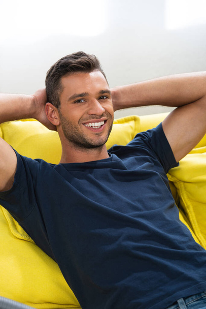 Young man smiling at camera while sitting on sofa at home  - Photo, Image