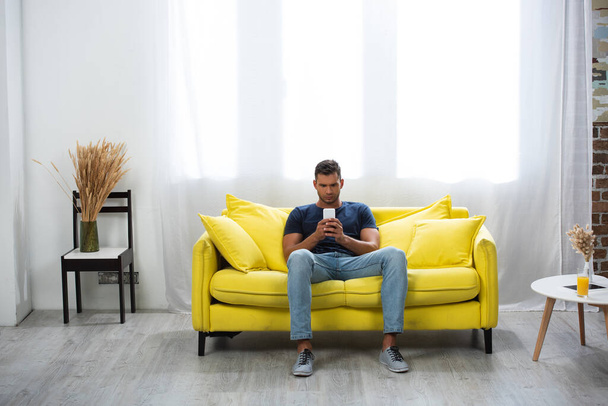 Man using smartphone on couch near glass of orange juice on coffee table  - Foto, imagen