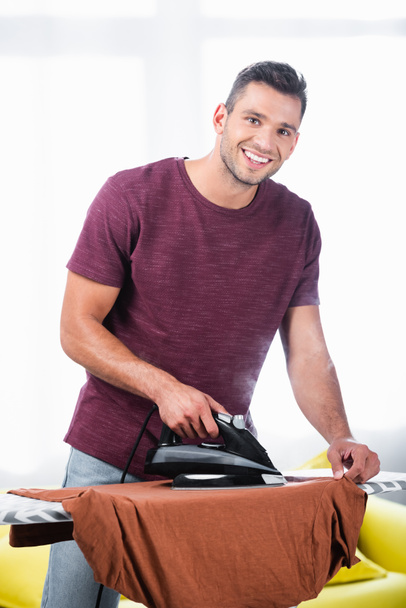 Cheerful man ironing clothes with steam on board at home  - Fotografie, Obrázek