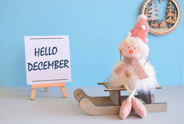 HELLO DECEMBER - Sneeuwpop met slee en winterdecoratie, blauwe achtergrond - Foto, afbeelding