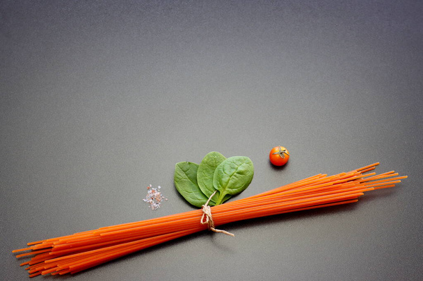Red spaghetti, green spinach leaves, cherry tomatoes and pink salt on a gray background. - Foto, immagini