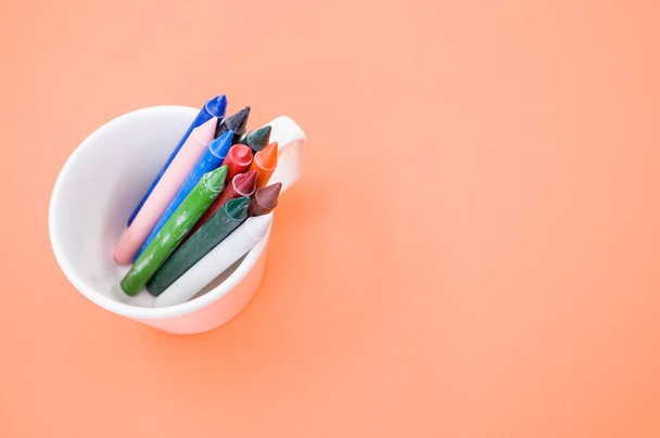 A top view of the colorful crayons in the cup on the orange surface - space for text - Foto, Imagem