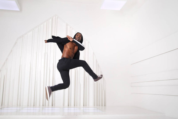 Элегантный черный танцор в черной одежде прыгает в яркой комнате. - Фото, изображение