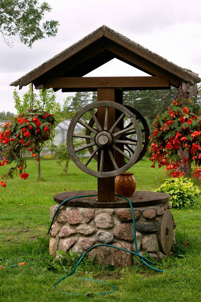 Régi klasszikus vízkút felújítása. A kút, amely díszített virágcserepek piros begónia - Fotó, kép