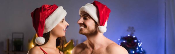 cheerful couple in santa hats looking at each other, banner - Photo, Image