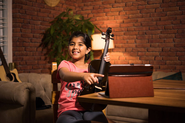 Aasian intialainen lapsi oppiminen musiikkia tai soitinta verkossa kannettavan tietokoneen tai tabletin kotona, vakuuttava harrastus - Valokuva, kuva