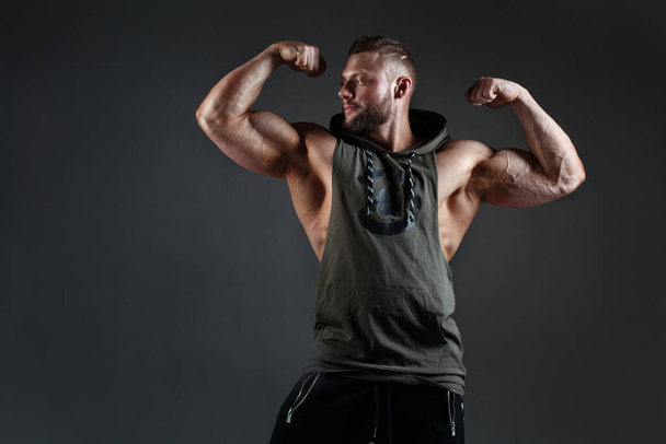 Muscular white man shows biceps against a dark background. - Photo, image