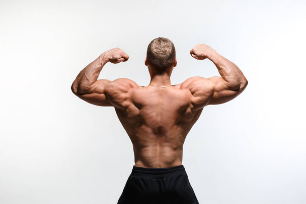 Muscular bodybuilder shows his muscles isolated on a white background, view from the back. - Фото, изображение