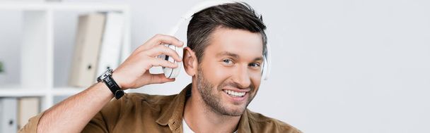 Hombre de negocios sonriente quitándose los auriculares mientras mira la cámara en un fondo borroso, pancarta - Foto, imagen