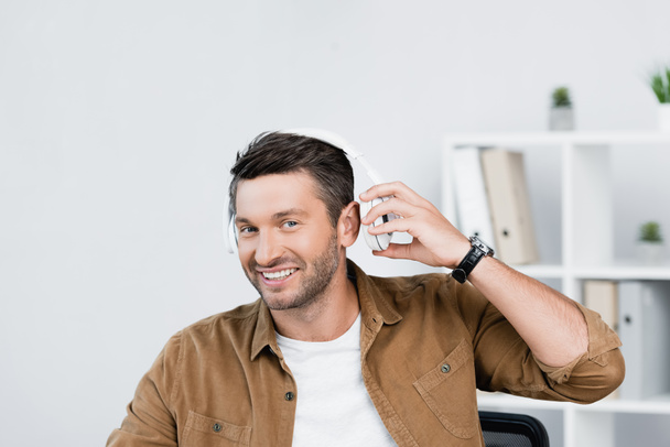 Веселый бизнесмен снимает наушники, глядя в камеру на фоне размытого офиса - Фото, изображение