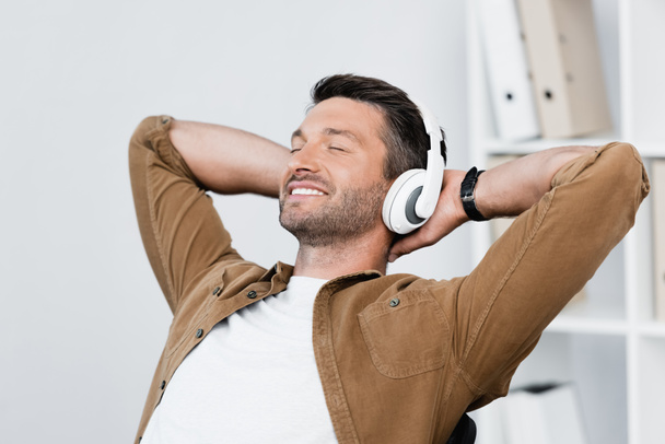 Mosolygó üzletember a fejhallgató pihentető, miközben zenét hallgat homályos háttérrel - Fotó, kép
