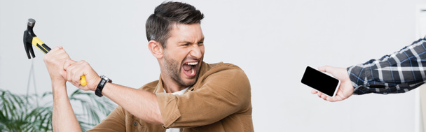 Θυμωμένος επιχειρηματίας με σφυρί φωνάζοντας κοντά smartphone στο χέρι του ανθρώπου, πανό - Φωτογραφία, εικόνα
