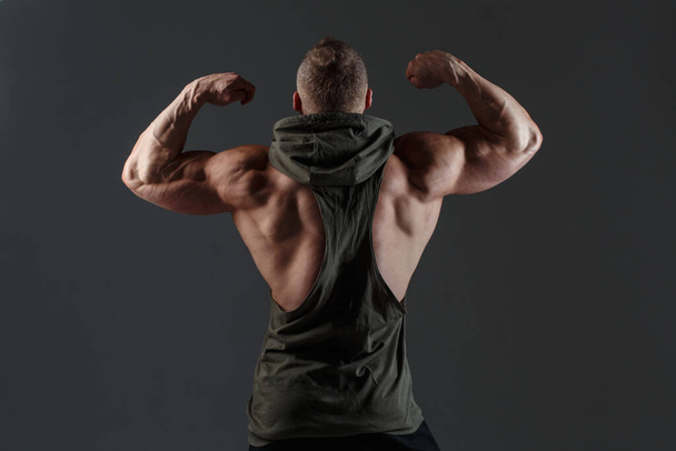 Athletic white man shows muscles view from the back against a dark background. - Fotografie, Obrázek