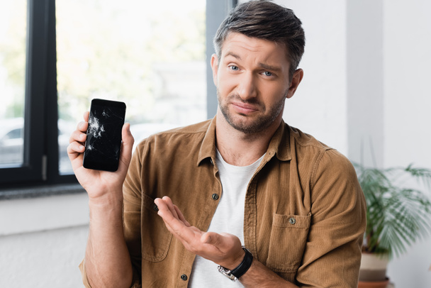 Skeptinen liikemies katselee kameraa osoittaessaan käsi murskattua älypuhelinta hämärtyneellä taustalla - Valokuva, kuva