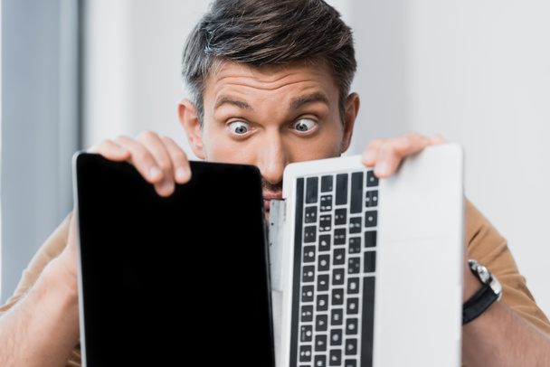 Удивлённый бизнесмен смотрит на сломанный ноутбук на размытом фоне - Фото, изображение
