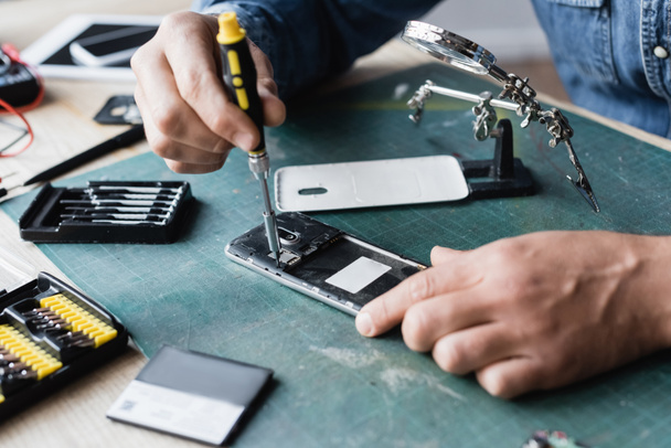 Cropped view of repairman with screwdriver fixing disassembled mobile phone at workplace on blurred background - Foto, immagini