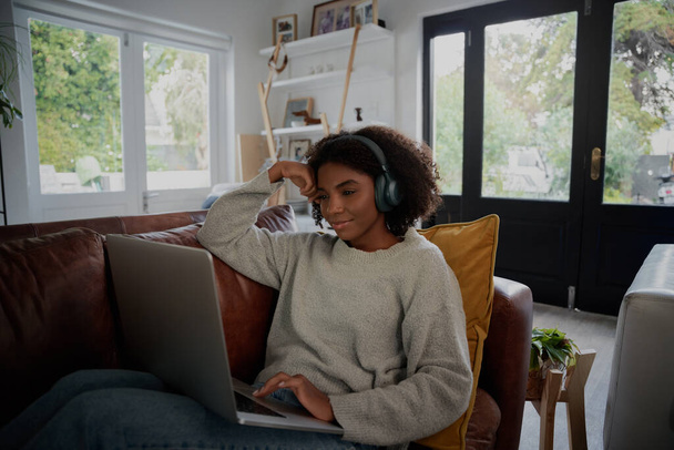 Young black student enjoying lockdown vacation by watching video on laptop with headphones at home - Photo, Image