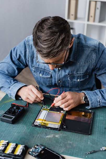 Reparateur mit Haltesensoren von Multimeter auf kaputtem Teil des digitalen Tablets am Arbeitsplatz - Foto, Bild