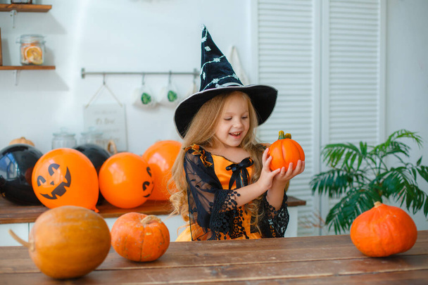 Little girl in a witch costume in the kitchen with pumpkins - Foto, Imagem