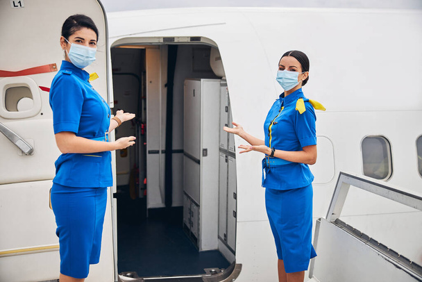 Stewardesses in face masks inviting passengers aboard - Foto, Imagem
