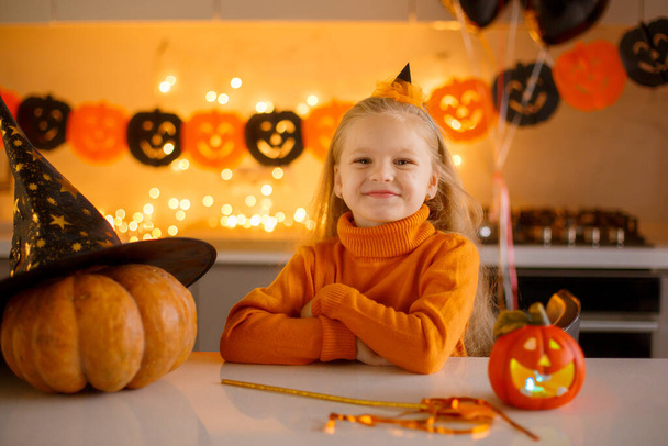 niña en Halloween en un traje de calabaza en casa en la cocina - Foto, Imagen