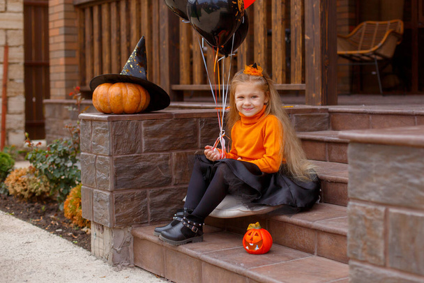 милая маленькая девочка сидит на крыльце с воздушными шарами, Хэллоуин концепции - Фото, изображение