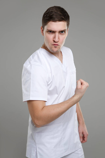 Young man in medical overalls demonstrates strength Isolated on a gray background. - Zdjęcie, obraz