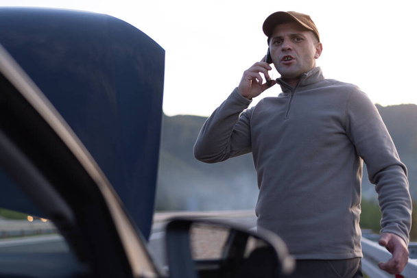 Frustrated and angry man calls roadside assistance by phone. car problem. Roadside assistance concept - Photo, Image