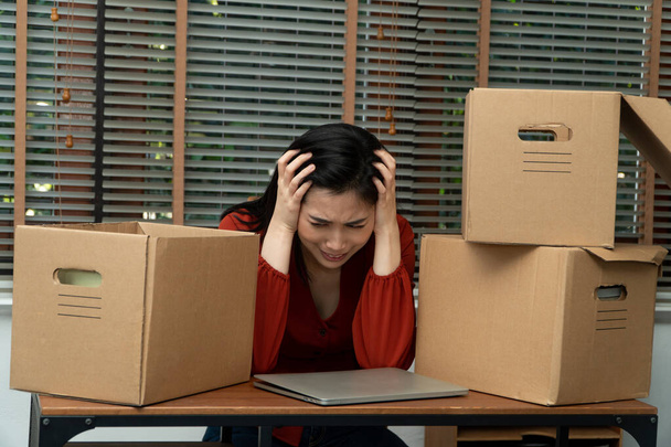 Traurige Asiatin, die Habseligkeiten in einen Karton packt und auf dem Schreibtisch im Büro weint, nachdem sie entlassen wurde und arbeitslos ist. Konzept der Auswirkungen auf den wirtschaftlichen Abschwung und Management des Scheiterns - Foto, Bild