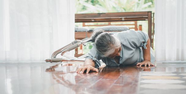 Ασιάτισσα ηλικιωμένη να πέφτει κάτω στο πάτωμα στο σπίτι, μετά να σκοντάφτει στο κατώφλι και να κλαίει από τον πόνο και να ζητάει βοήθεια. Έννοια της ασφάλισης γήρατος και της υγειονομικής περίθαλψης - Φωτογραφία, εικόνα