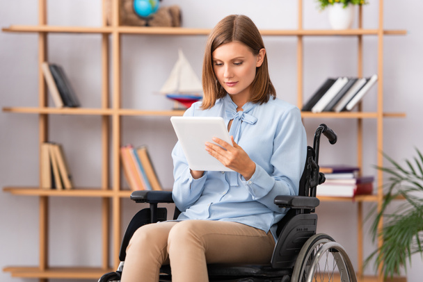 Female psychologist using digital tablet while sitting in wheelchair with blurred office on background - 写真・画像