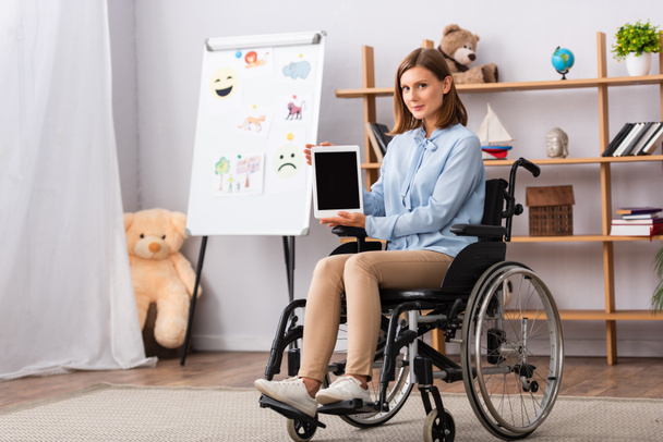 Full length of female psychologist showing digital tablet while sitting in wheelchair in office - 写真・画像