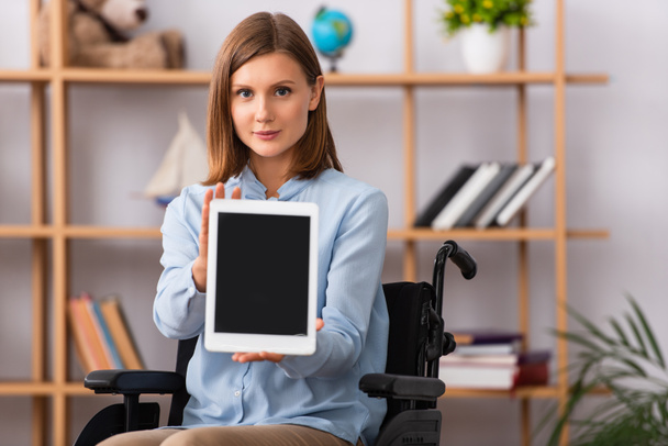 Psicóloga positiva mostrando tableta digital sentada en silla de ruedas sobre fondo borroso - Foto, imagen