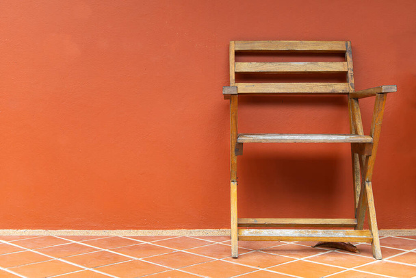 Drewniane krzesła na podłodze z terakoty i pomarańczowe ściany tynkowe tło, drewniane krzesła na balkonie. - Zdjęcie, obraz