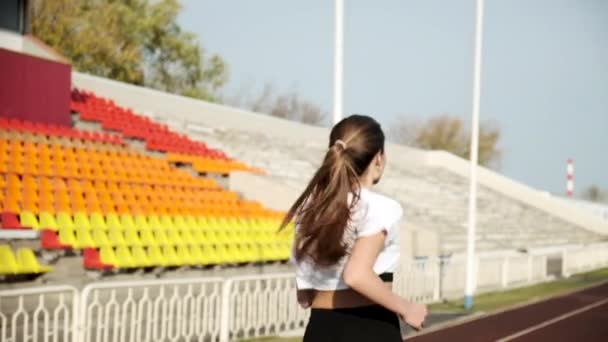 Acompanhamento do jovem corredor de fitness em sportswear correndo na pista do estádio - Filmagem, Vídeo