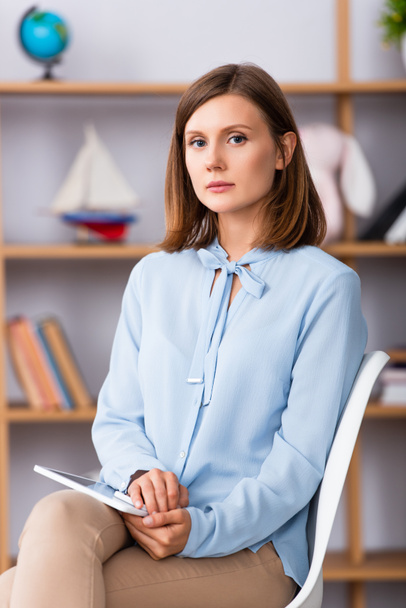 Female psychologist with digital tablet looking at camera while sitting on chair on blurred background - Photo, Image