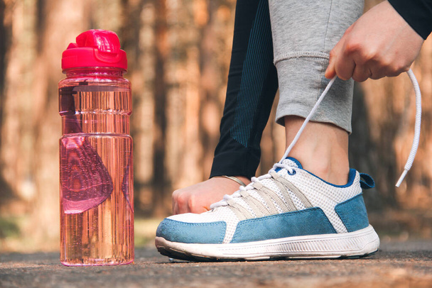The girl ties the laces of her sneakers. Sports shoes and sports bottle close up - Foto, immagini