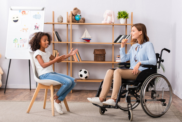 Happy african american gesturing while talking to psychologist in wheelchair at office - Foto, Bild