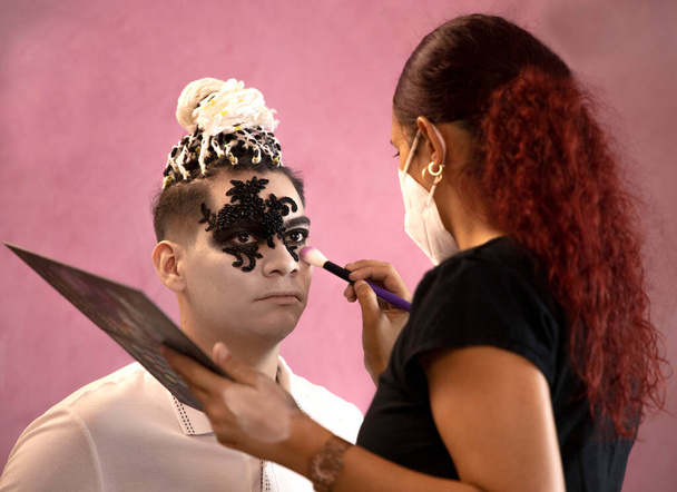 Художник-гример в маске рисует лицо мужчины на Хэллоуин - Фото, изображение