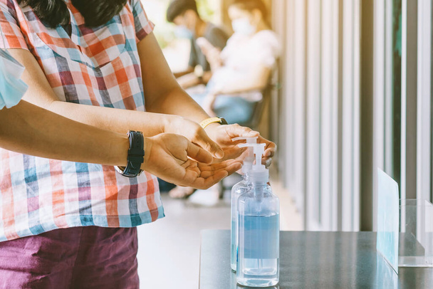 Frauenhände drückten vor dem Betreten des Coffeeshops eine blaue Alkoholgelflasche, um die Ausbreitung des Coronavirus (Covid-19) zu verhindern. Neuer normaler Lebensstil. Selektiver Fokus auf Alkohol-Gel-Flasche. - Foto, Bild