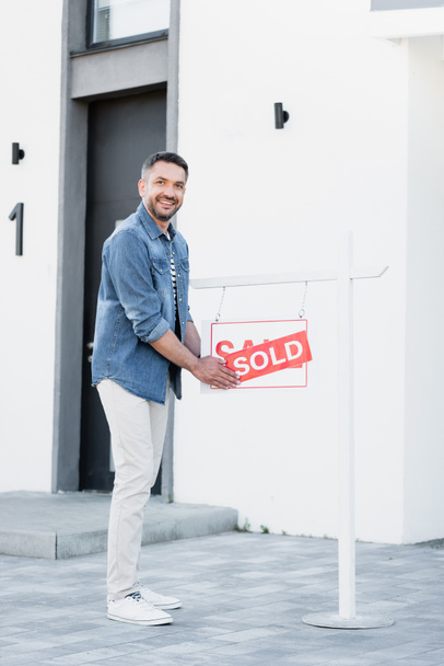 Full length of smiling man holding sign with sold lettering near house - Photo, Image