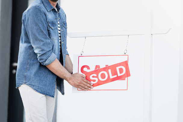 Widok człowieka trzymającego znak ze sprzedawaną literą w pobliżu domu na rozmytym tle - Zdjęcie, obraz