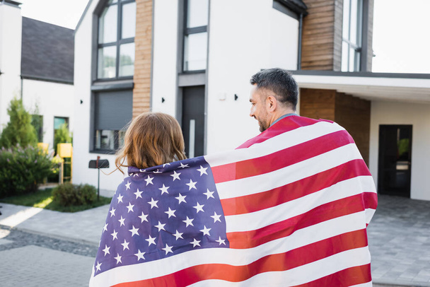 Back view of couple covered with american flag near house on blurred background - Photo, Image