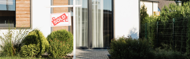 Fachada frontal de casa moderna cerca de césped y letrero con letras vendidas, pancarta - Foto, imagen