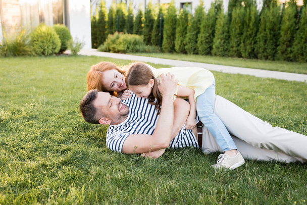 Famille heureuse riant tout en étant allongé sur la pelouse sur fond flou - Photo, image