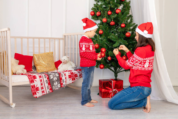 matka a dítě zdobí vánoční stromeček před novým rokem nebo Vánoce v dětském pokoji s novoroční interiérem - Fotografie, Obrázek