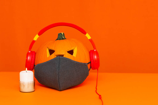 Fron view Happy Halloween decoraties festival en muziek concept achtergrond.Mix verscheidenheid kaars items gezichtsmasker en pompoen luisterradio door hoofdtelefoon op oranje achtergrond. - Foto, afbeelding